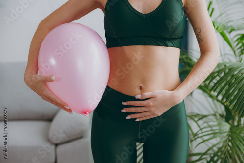 Cropped close up young strong sporty athletic fitness trainer instructor woman wear green tracksuit training hold balloon near belly do exercises at home gym indoor. Workout sport motivation concept. photo