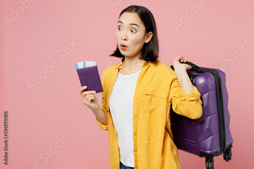 Traveler sad woman wears casual clothes hold suitcase passport ticket isolated on plain pastel pink background. Tourist travel abroad in free spare time rest getaway Air flight trip journey concept. #586893086