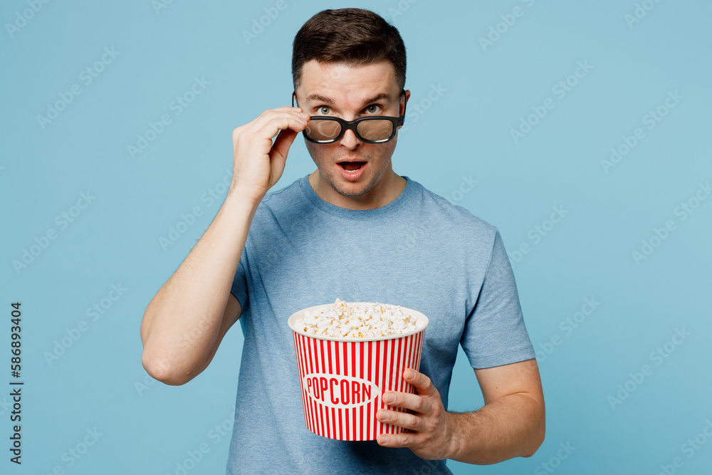 Young shocked surprised amazed impressed man lower 3d glasses wear casual t-shirt watch movie film hold bucket of popcorn in cinema look camera with opened mouth isolated on yellow background studio.