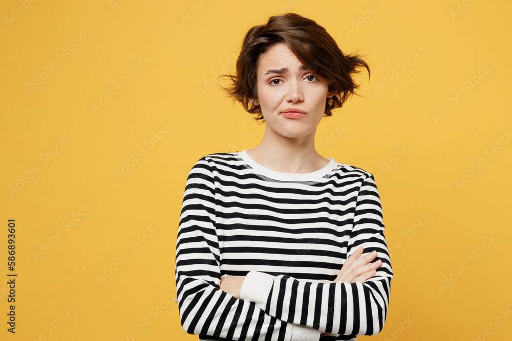 Young sad grumpy frustrated dissatisfied displeased woman wearing casual striped black and white shirt look camera hold hands crossed folded isolated on plain yellow color background studio portrait. Young sad grumpy frustrated dissatisfied displeased woman wearing casual striped black and white shirt look camera hold hands crossed folded isolated on plain yellow color background studio portrait.
