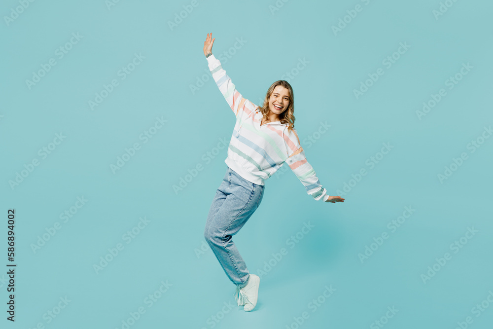 Full body cheerful fun young woman wear striped hoody stand on toes leaning back with outstretched hands dance isolated on plain pastel light blue cyan background studio portrait. Lifestyle concept.
