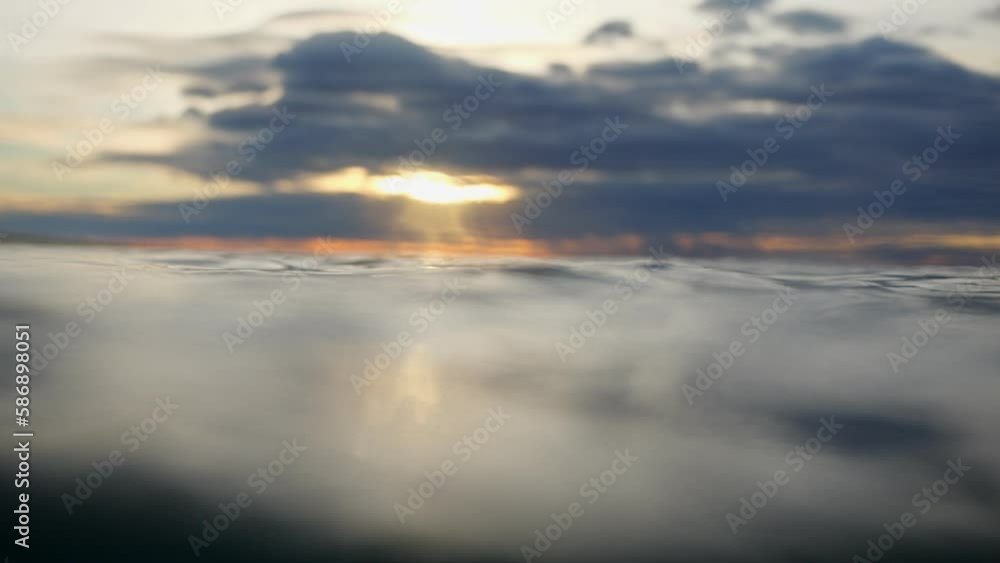 Balancing above the surface of the water, the camera sinks under the water. The sun low over the water is reflected in the waves. Diving at sunrise. Balancing above the surface of the water, the camera sinks under the water. The sun low over the water is reflected in the waves. Diving at sunrise.