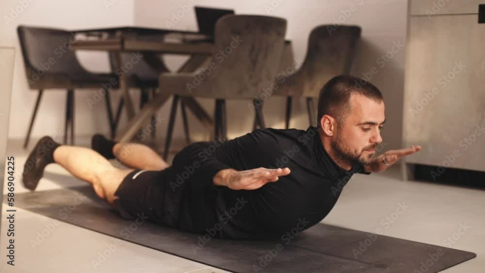 Stretching training. Young man wear black sport clothes and exercising on fitness mat at home. Sporty man in shorts doing yoga indoors. Stretching training. Young man wear black sport clothes and exercising on fitness mat at home. Sporty man in shorts doing yoga indoors.