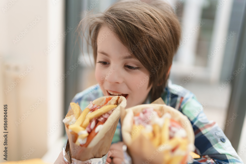 Cute little boy biting gyro sandwich. Handsome young kid eating traditional Greek fast food in a cafe Cute little boy biting gyro sandwich. Handsome young kid eating traditional Greek fast food in a cafe