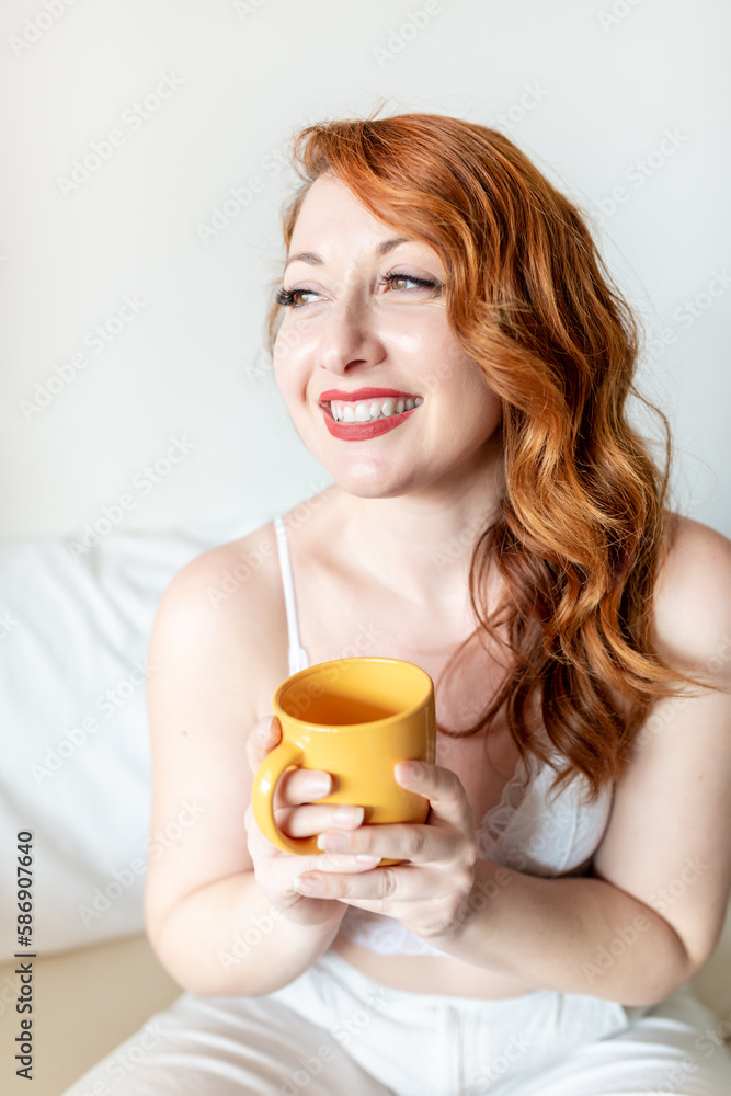 Happy young woman with confident attitude, redhead and caucasian skin looking at the horizon with a yellow mug sitting on the bed
Happy young woman with confident attitude, redhead and caucasian skin looking at the horizon with a yellow mug sitting on the bed