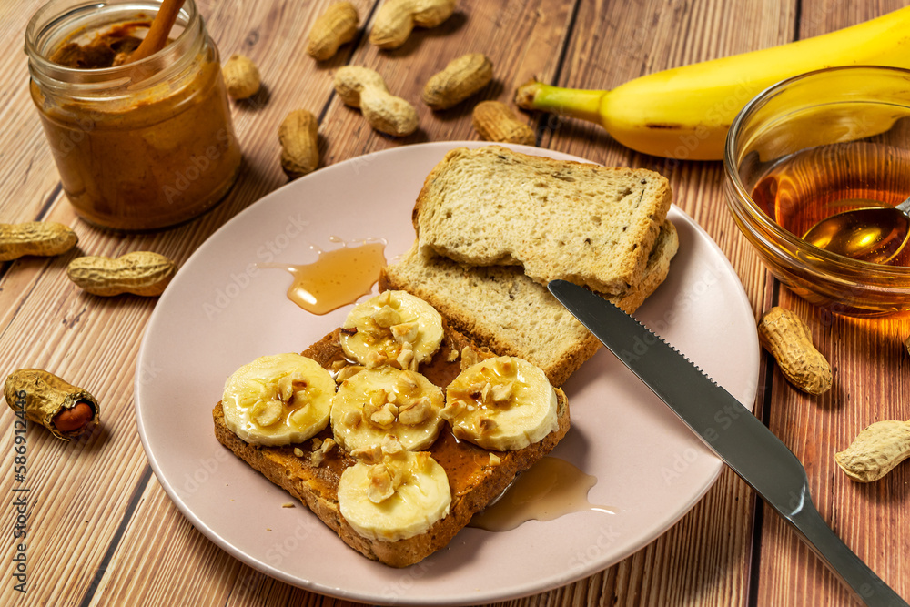 Peanut butter or peanut paste in an open jar and spread on a toast sandwich with banana and honey and peanuts in shells scattered on the table Peanut butter or peanut paste in an open jar and spread on a toast sandwich with banana and honey and peanuts in shells scattered on the table