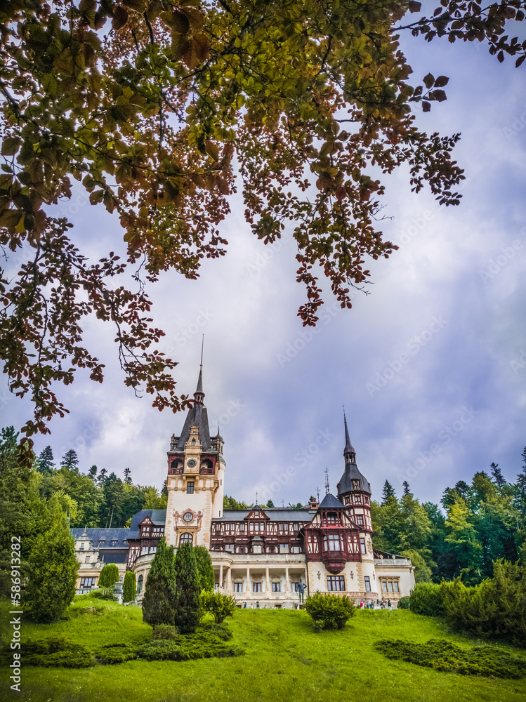 Front View Of The Peles Castle, Park With Trees And Bushes In The Foreground