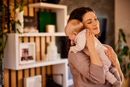 Tablou pe pânză A caring mother holding her little baby in her arms after eating at home