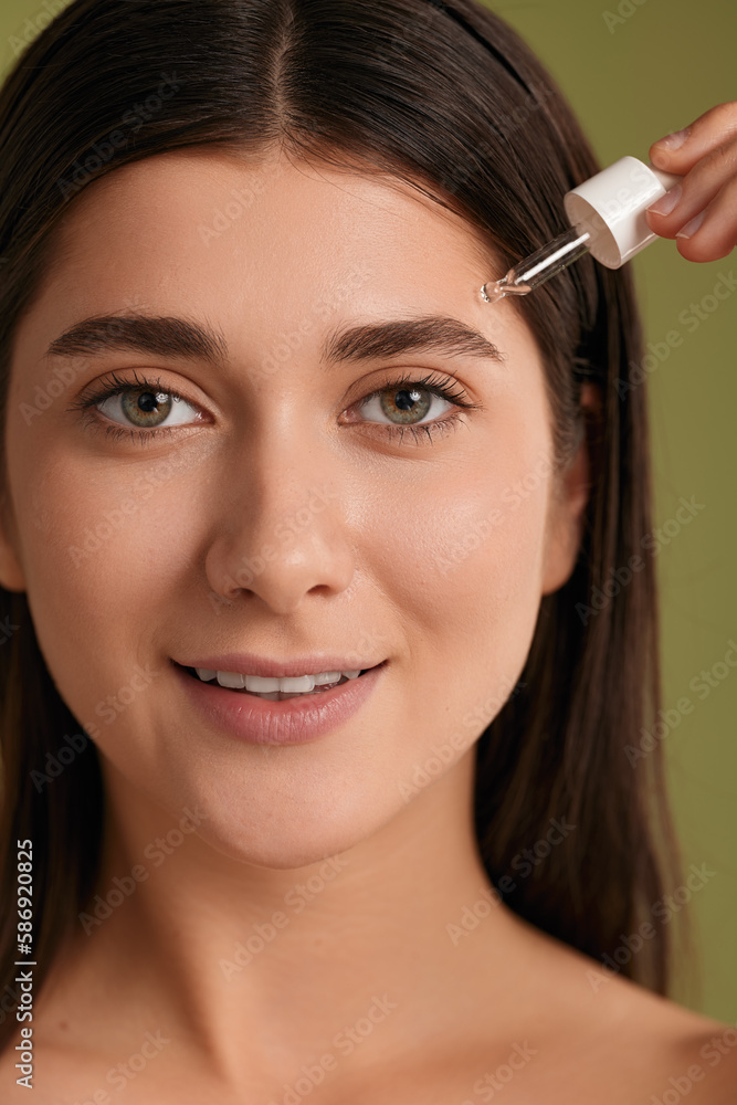 Smiling young lady applying oil serum on face during beauty routine Smiling young lady applying oil serum on face during beauty routine