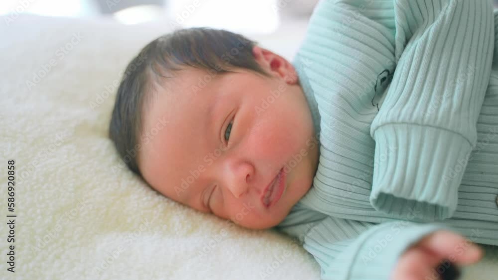 Newborn baby infant with dark hair lying on side sleeping awaking open eyes. Cute little Middle eastern child on blanket. Tranquil scene close up Newborn baby infant with dark hair lying on side sleeping awaking open eyes. Cute little Middle eastern child on blanket. Tranquil scene close up