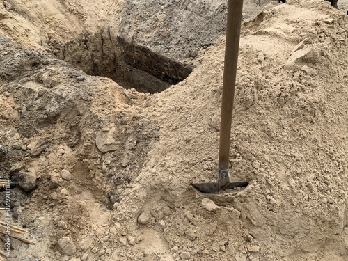 A hole dug in the ground with a shovel nearby. Place in the sand at the cemetery. Burial grave dug with a shovel. photo