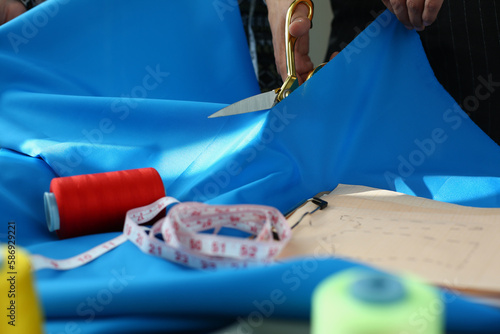 Girl cuts blue fabric with scissors on table in atelier. Tailoring fashionable stylish clothes in fashion studio