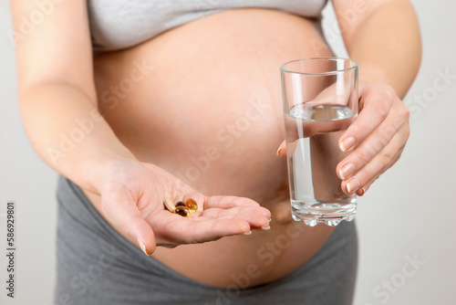 A pregnant girl holds pills and glass of water. The benefits of vitamins for mother and child.