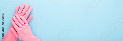 Female hands in pink rubber protective gloves on light blue table background. Pastel color. Closeup. Point of view shot. Wide banner. Empty place for text. Top down view.