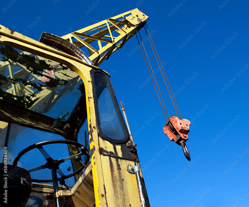 Fototapeta premium Old yellow battered crane with boom and hook against the blue sky.