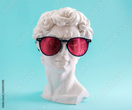Fotografie Plaster statue head wearing pink sunglasses on blue background.