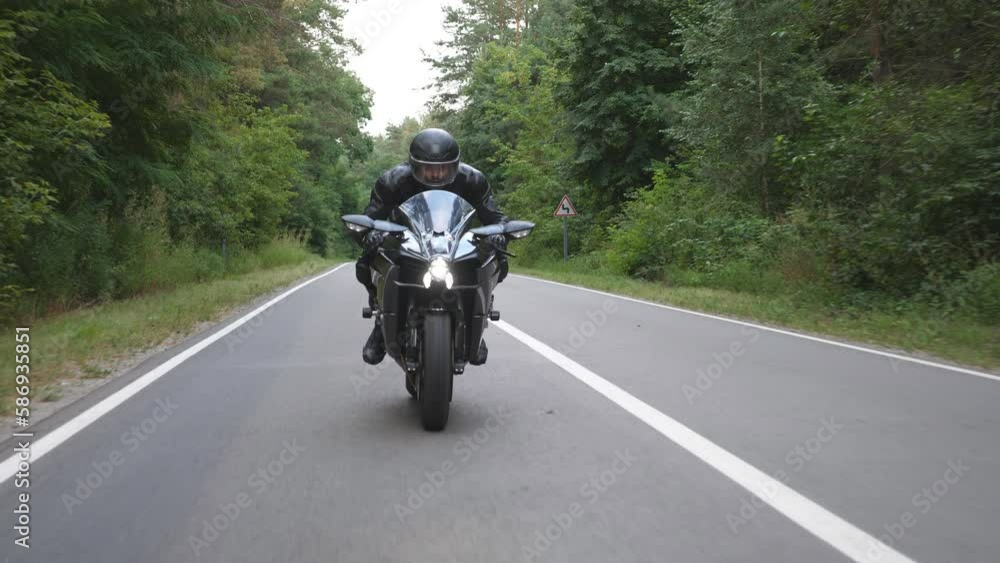 Young man in helmet riding on modern sport motorbike at rural forest road. Motorcyclist racing his motorcycle on wood route. Guy driving bike during trip. Concept of freedom and adventure. Front view Young man in helmet riding on modern sport motorbike at rural forest road. Motorcyclist racing his motorcycle on wood route. Guy driving bike during trip. Concept of freedom and adventure. Front view