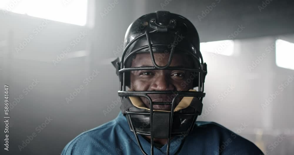 Portrait of handsome African American man glancing at camera. Attractive player with helmet and sports outfit happy and smiling in shadow gym club. Concept of sport, game, match, challenge. Portrait of handsome African American man glancing at camera. Attractive player with helmet and sports outfit happy and smiling in shadow gym club. Concept of sport, game, match, challenge.