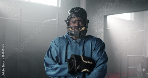 Portrait of good-looking African American man wearing gloves, helmet and sports uniform, standing in front of camera. Attractive male preparing to match in American football. Sport concept. photo