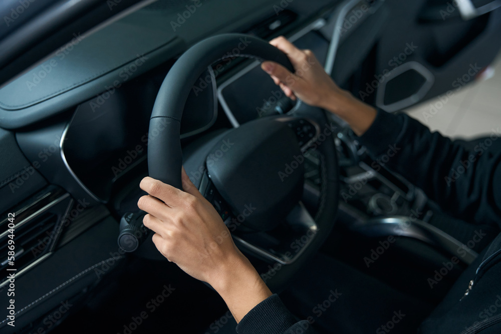 Hands of a young woman lie on the steering wheel