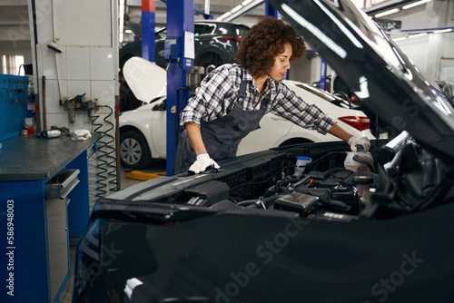 Multiracial female auto repairman looks under hood glass washer reservoir