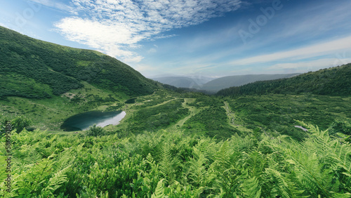 Lake on green mountains valley. Blue sky with white clouds. Rewilding and recreation concept.