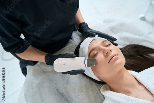 Cosmetologist holding instrument and cleaning skin, working in salon
