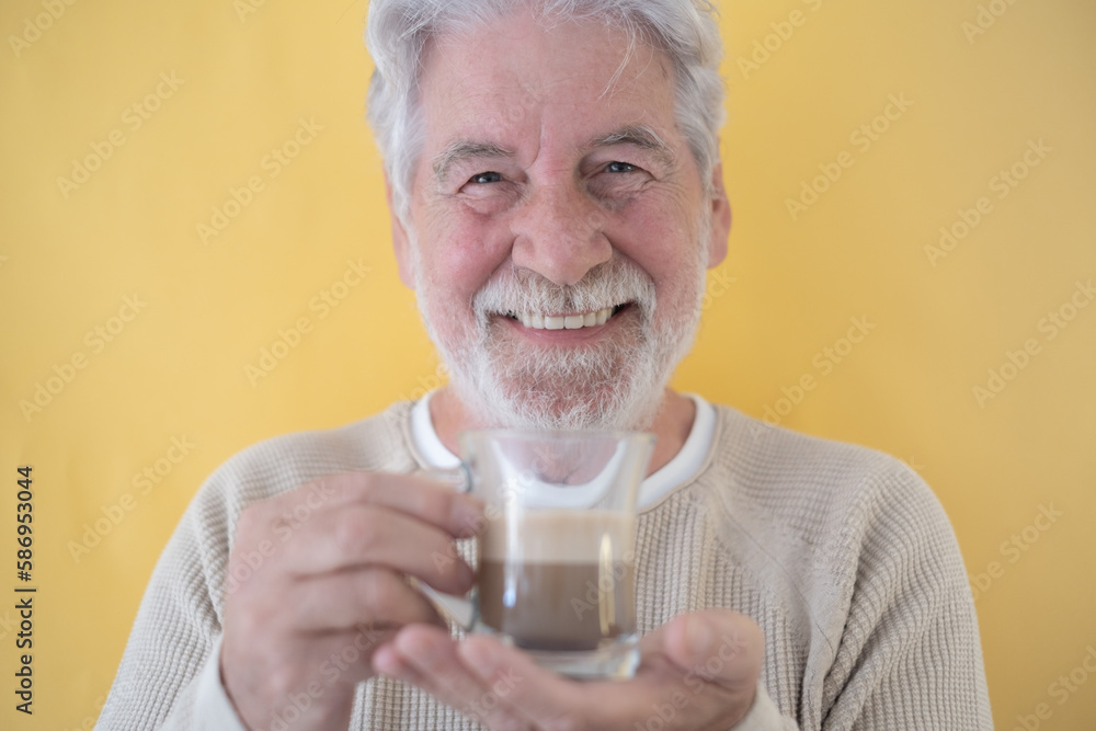 Portrait of Smiling Senior Bearded Man Holding a Glass of Coffee and Milk, Cappuccino Looking at Camera, on Yellow Background Portrait of Smiling Senior Bearded Man Holding a Glass of Coffee and Milk, Cappuccino Looking at Camera, on Yellow Background