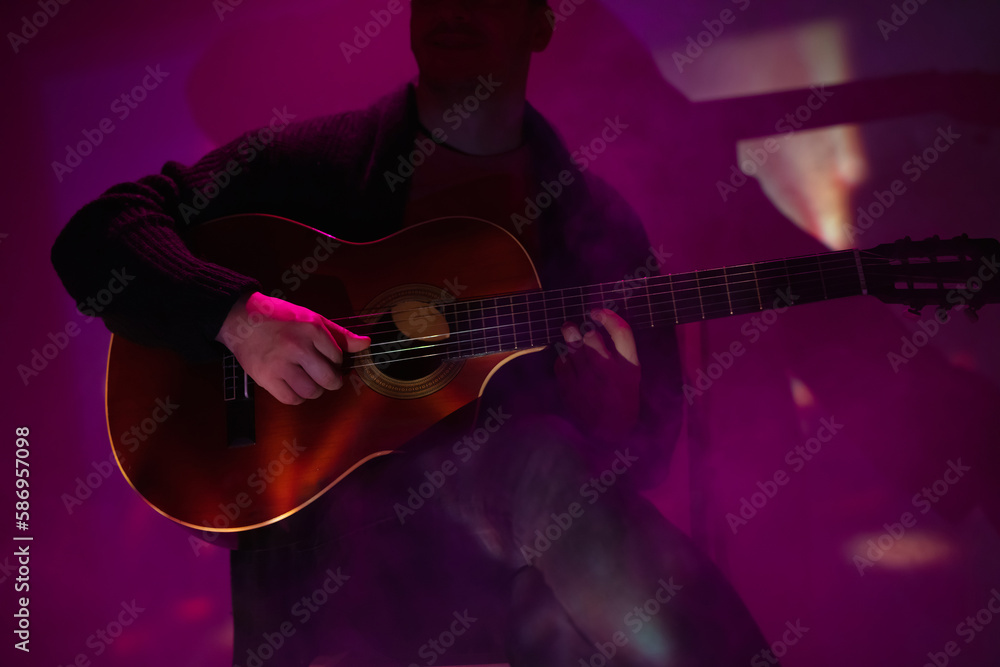 Obraz premium Musician playing acoustic guitar in a foggy club with colorful lights.