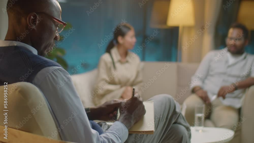 Selective focus shot of black male therapist taking notes and talking to married couple as they arguing during counseling session Selective focus shot of black male therapist taking notes and talking to married couple as they arguing during counseling session