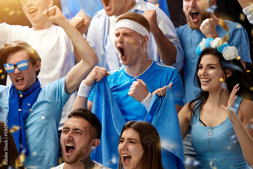 Happy and excited people, sport fans emotionally cheering up favourite football, soccer team of greece at stadium during game. Concept of sport, leisure time, emotions, hobby and entertainment