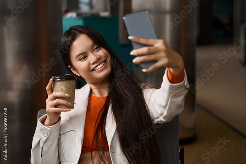 Cheerful female office worker taking selfie during coffee break