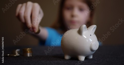 defocused child puts a coin in a white piggy bank, a little girl learns to save money for big purchases.