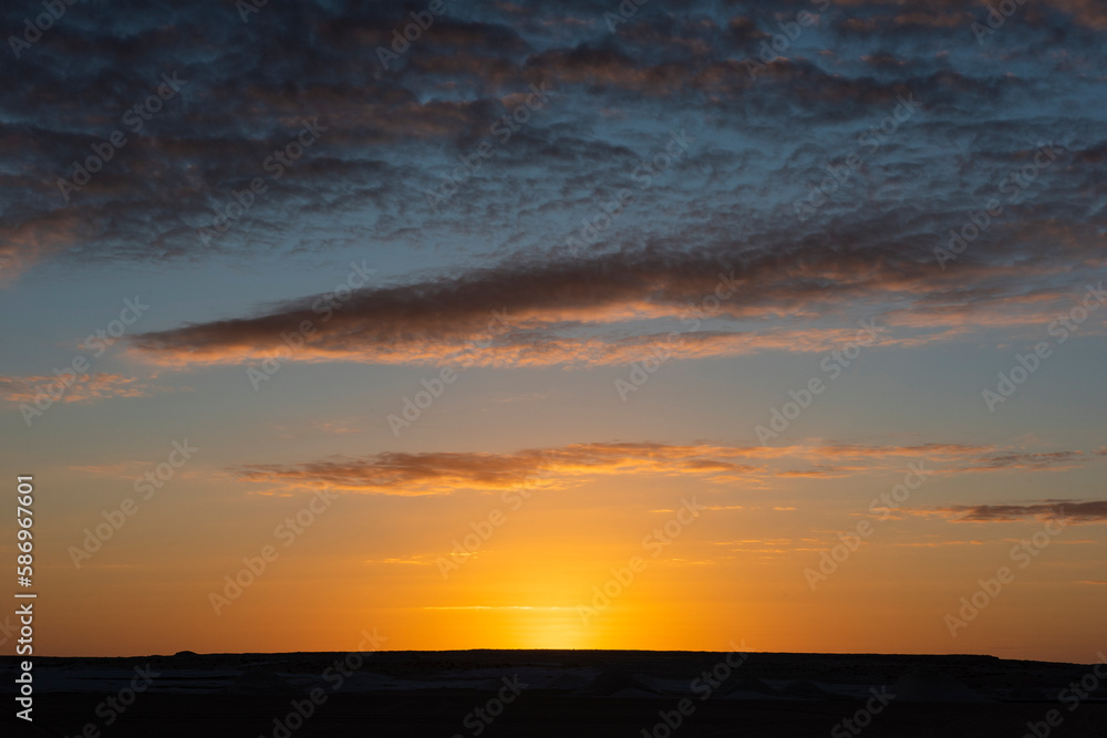 Barren desert landscape with sunrise in cloudy sky