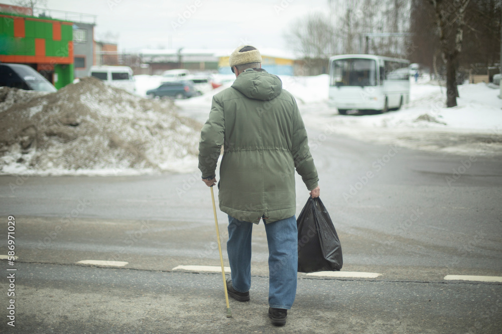 Man with walking stick. Person crosses road. Pensioner carries bag of groceries.