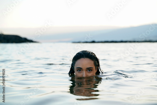 Mystery woman swimming in the ocean , looking at the camera with her big beautiful eyes.  Portrait of calm girl. © neonshot