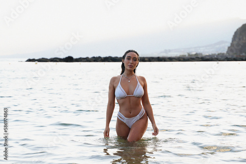 Attractive woman with beautiful body wearing white fashionable bikini posing in the ocean  looking at the camera. Island girl.