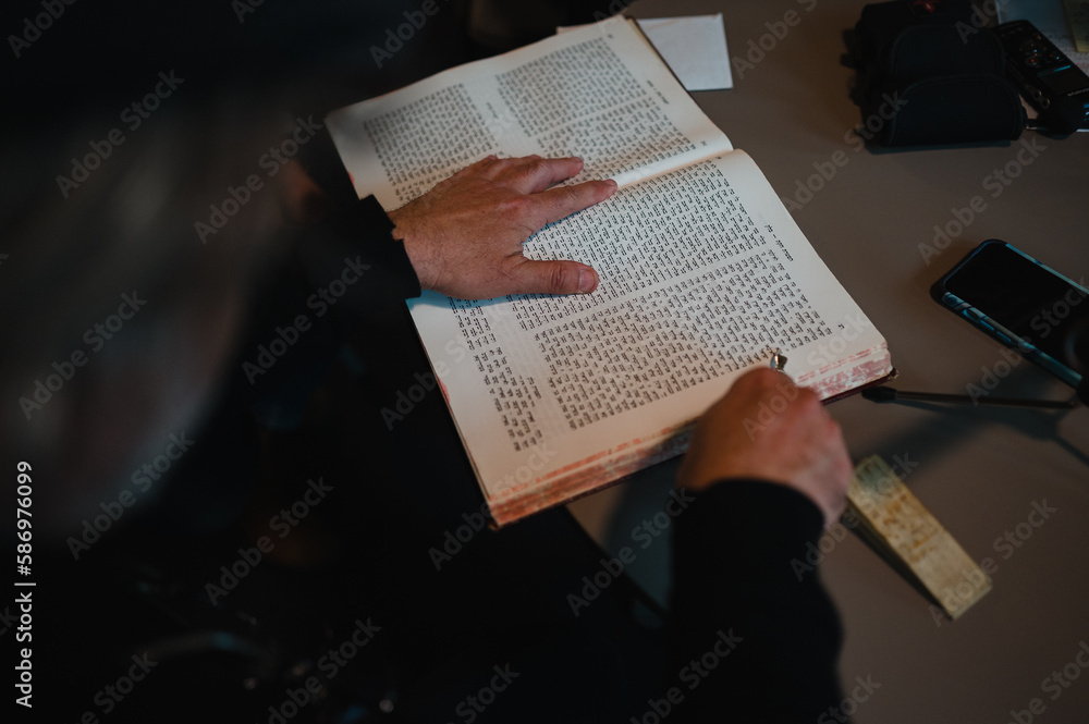 Naklejka premium Eine Person blättert durch ein religiöses Buch mit hebräischen Schriftzeichen und nutzt einen Zeiger für die Lesung