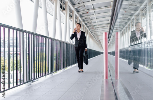 young Asian businesswoman in black suit using digital tablet and standing on walkway station with copy space. © anusak