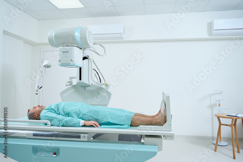 Man lying on bed waiting for X-Ray machine to scan for injury