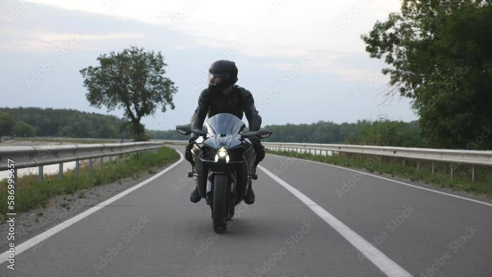 Young man travelling on a motorbike. Biker ride at dam road near lake or river. Motorcyclist driving his motorcycle on country route during journey. Concept of freedom and adventure at trip. Close up Young man travelling on a motorbike. Biker ride at dam road near lake or river. Motorcyclist driving his motorcycle on country route during journey. Concept of freedom and adventure at trip. Close up