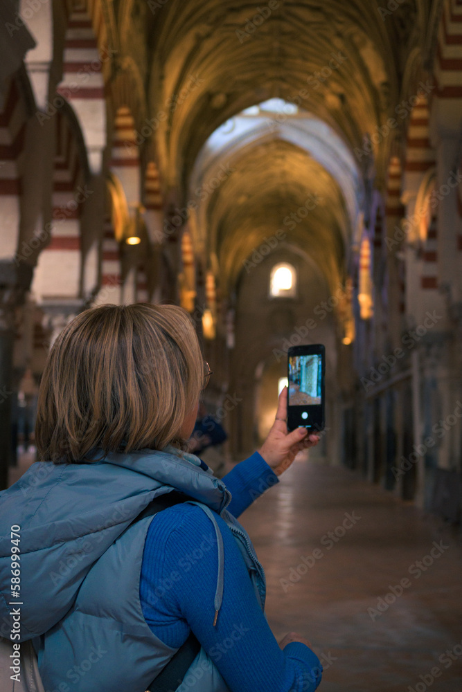 Middle-aged woman takes a photo with her mobile phone in the interior of a cathedral Middle-aged woman takes a photo with her mobile phone in the interior of a cathedral