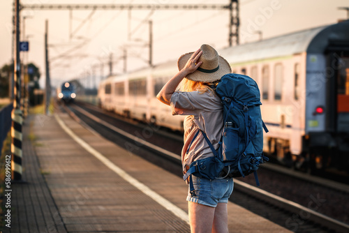 Travel by train. Woman backpacker standing at railroad station and looking at arriving train
