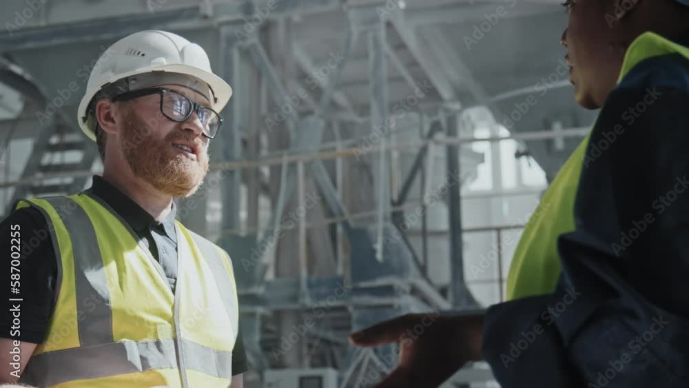 Low angle of African American and Caucasian co-workers in uniform standing in marble factory workshop discussing something Low angle of African American and Caucasian co-workers in uniform standing in marble factory workshop discussing something