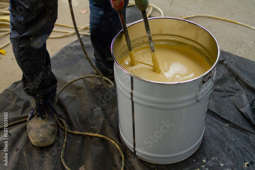 The worker is carefully mixing epoxy composites in a metal bucket to create high-quality polyurethane resin. 