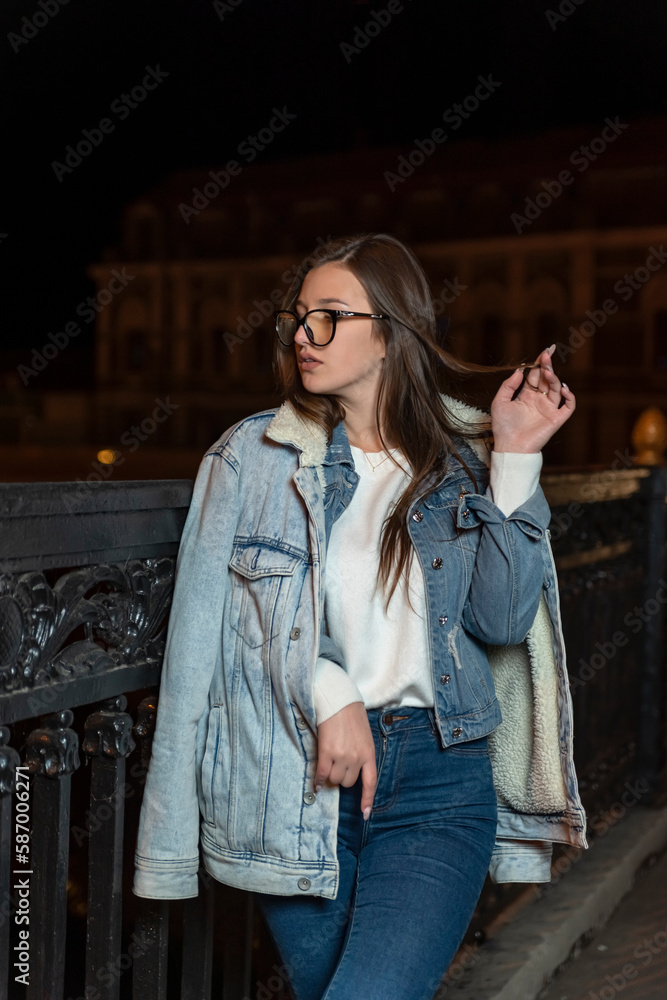 Stylish girl walk on night city street. Young girl in casual style on evening city background. Vertical frame