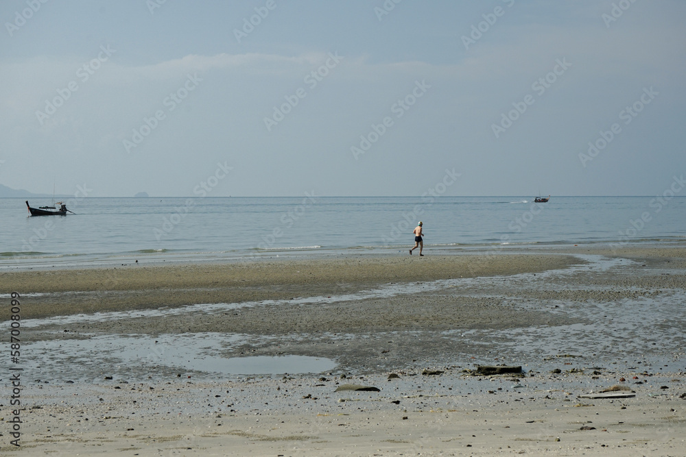 Healthy man runs alone along the beach with horizontal line of seascape and parking boats in background