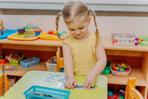 little cute toddler kid girl child in a yellow dress playing with toys puzzles in kindergarden. early development and montessory method of learning photo