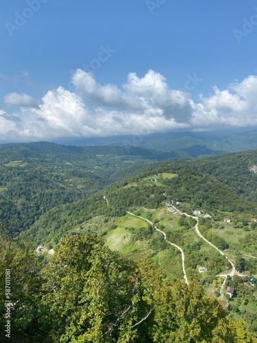 Landscape of a mountainous area with green slopes, trees, spring flowers and a blue sky with white clouds.