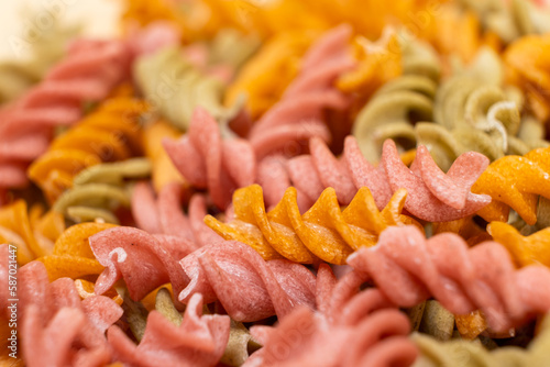 Rice vegetable pasta in the form of spirals, top view. Healthy rice pasta with tomatoes, selenera, carrots and beets photo